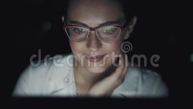 带眼镜的监视器屏幕的反射。 在办公室工作到很晚的年轻妇女